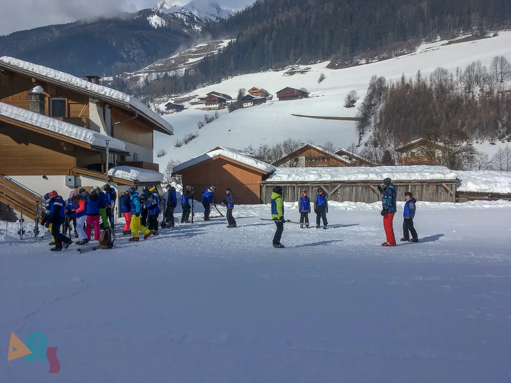 Skigruppe sammelt sich vor einem Holzgebäude.